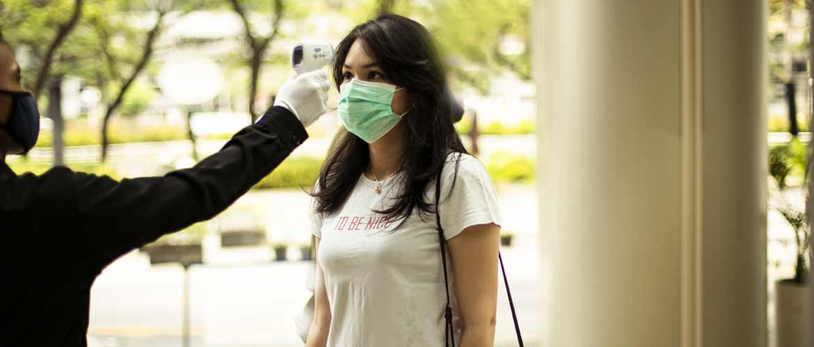 an employee wearing a face mask having her temperature taken before entering a building