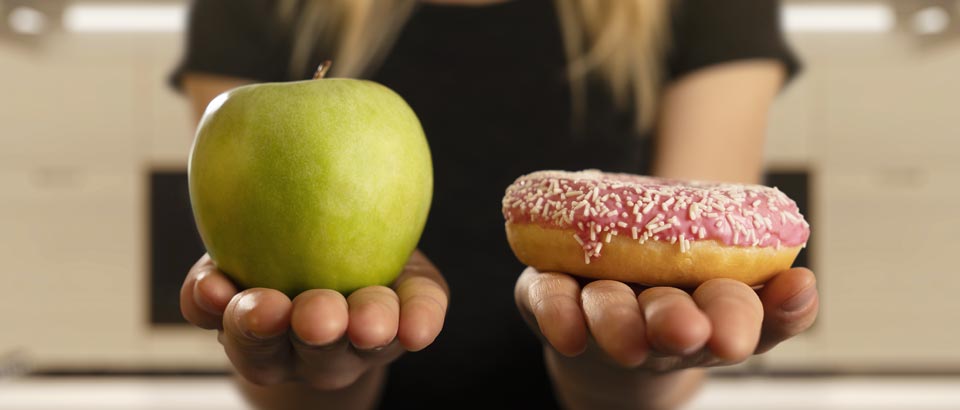 woman holding out an apple in one hand and a sprinkled donut in the other