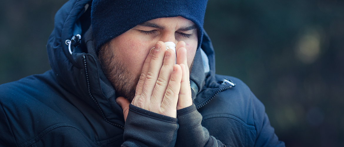 a man dressed in winter outerwear blowing his nose into a tissue
