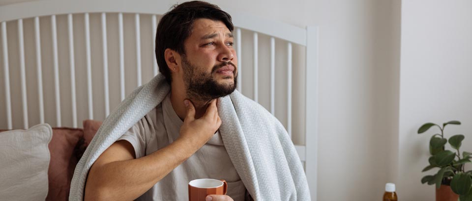man soothing throat with hand and mug of tea