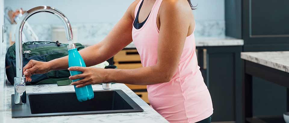 woman filling steel water bottle at sink