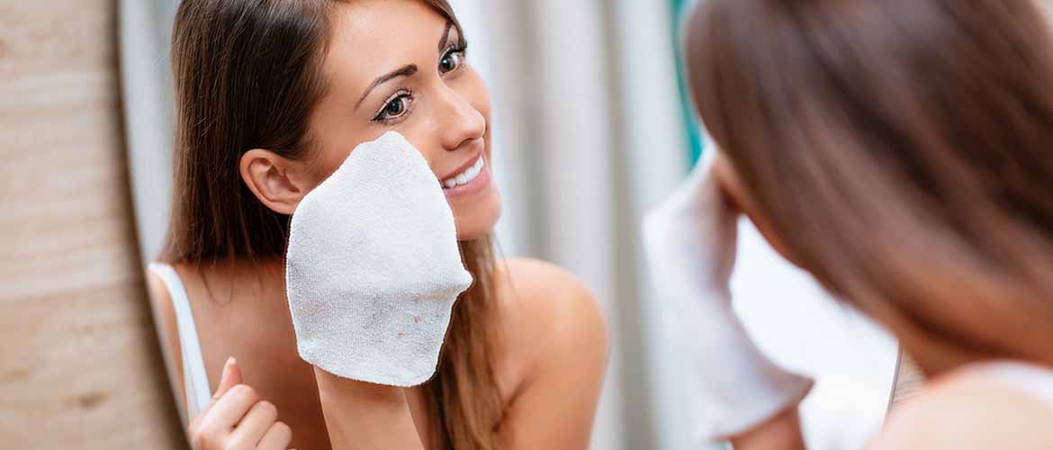 a woman removing makeup from her face with a washcloth