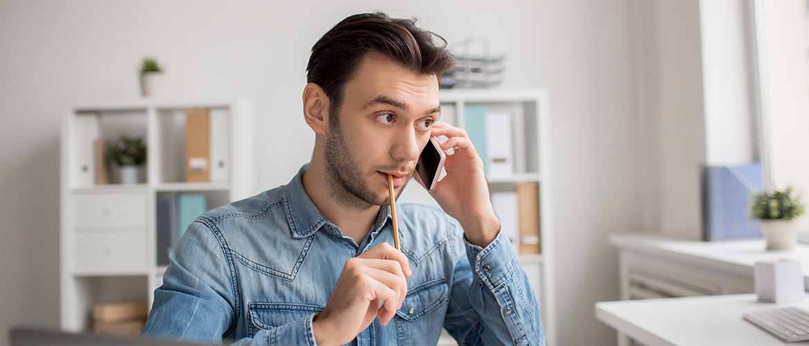 a man chewing on a pencil's eraser while holding a phone to his ear