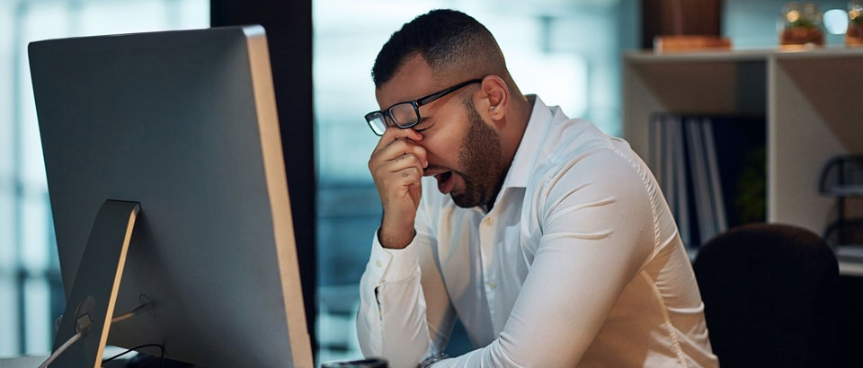 man sitting at a computer and rubbing his eyes