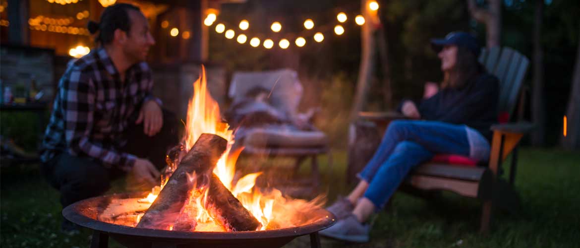 a man and woman sitting outside next to a campfire