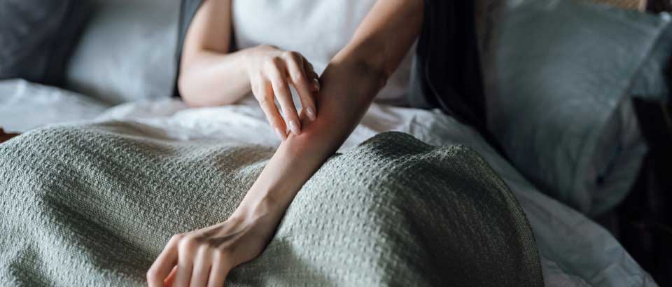 person sitting in bed scratching arm