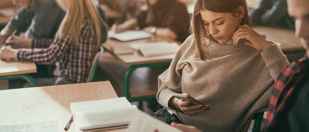 a woman looking at her cellphone while sitting in a classroom surrounded by other students