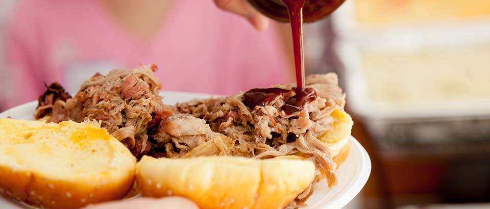 a person pouring barbeque sauce over a pulled pork sandwich