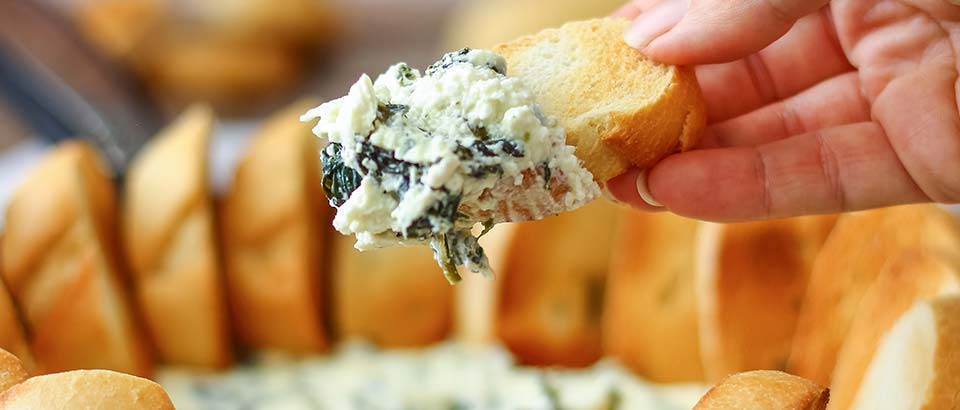 a person scooping up spinach and artichoke dip with a piece of bread
