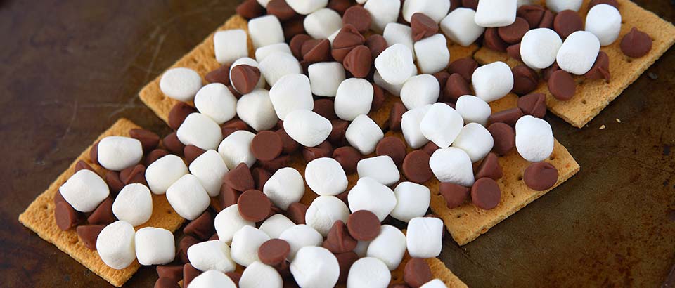 a tray of graham crackers with chocolate chips and marshmallows on top