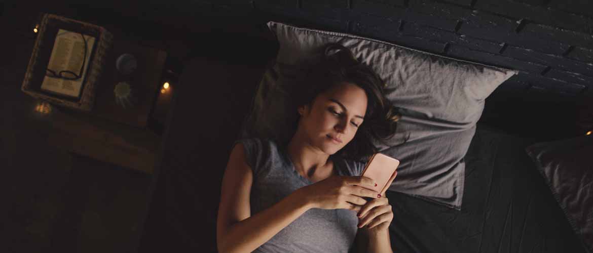 a woman lying in bed while looking at her phone