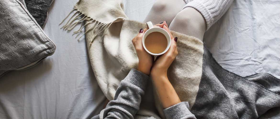 person holding a cup of tea in bed