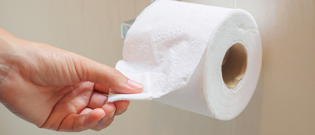 a person pulling a sheet off a toilet paper roll in a bathroom