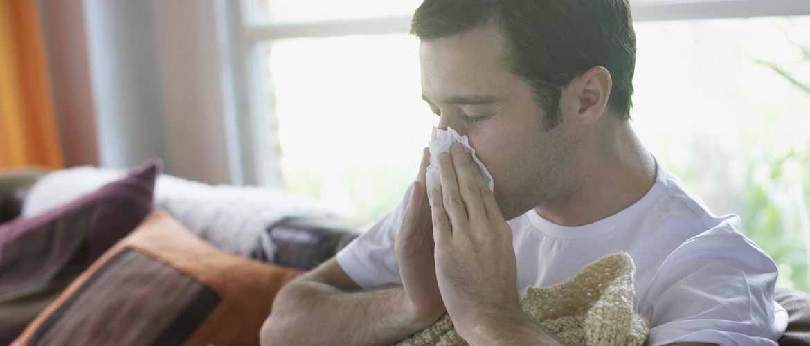a man sitting on a couch blowing his nose into a tissue