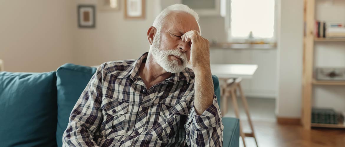 an older man holding his head in pain while sitting on a sofa