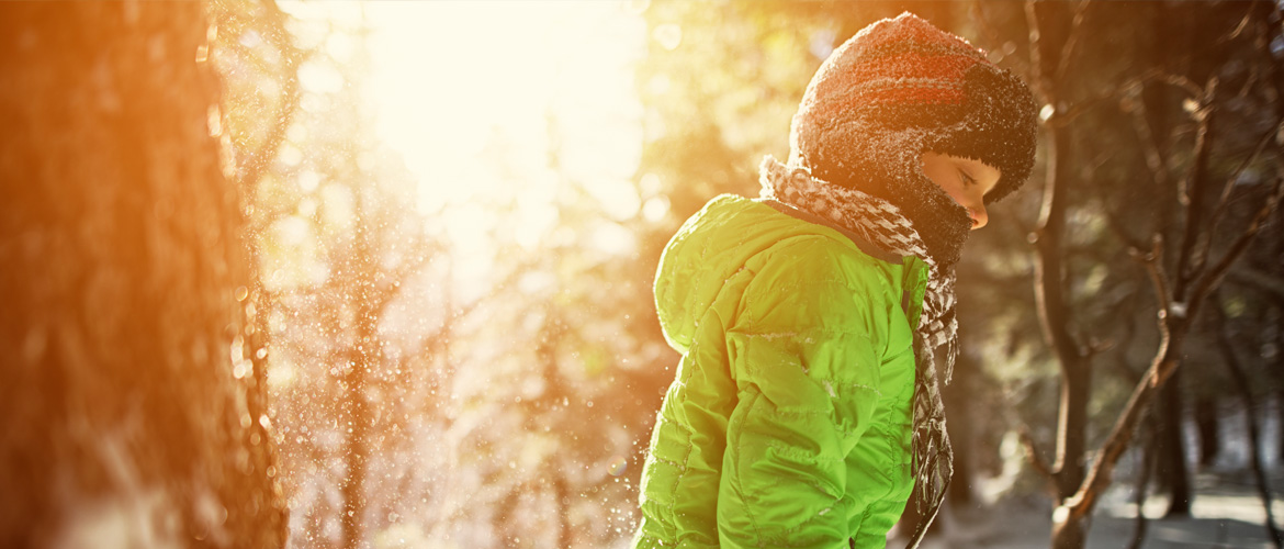 A young child outdoors in the snow wearing a heavy lime green jacket and fleece beanie face mask