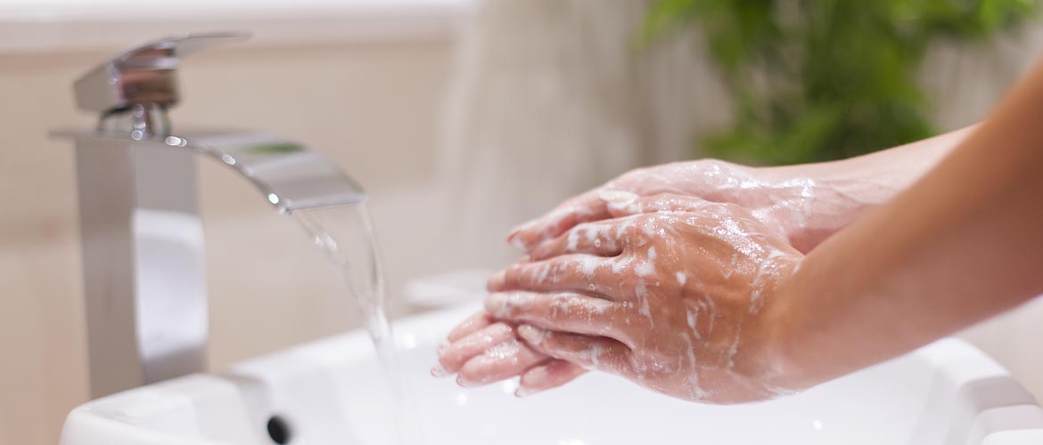 Hands covered in soapy lather at a sink with water running from the faucet