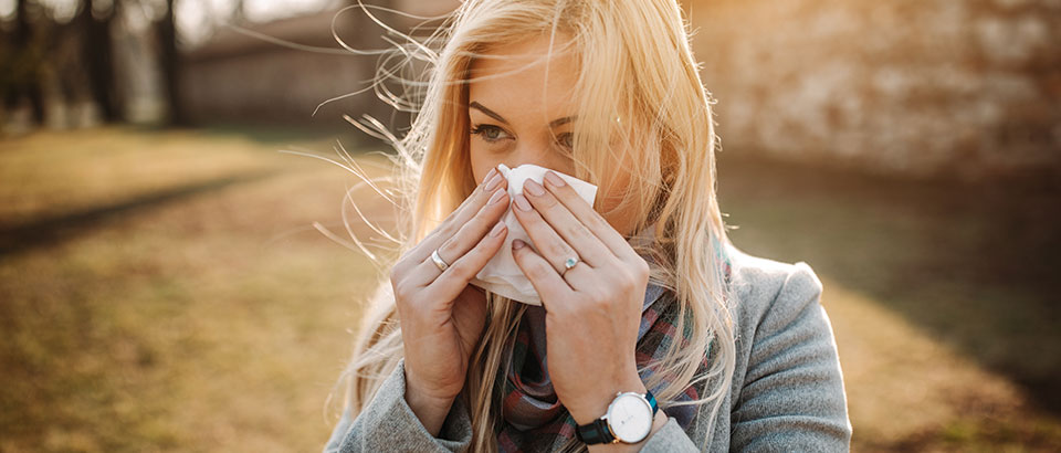 a woman sick with the flu blowing her nose into a tissue while outside