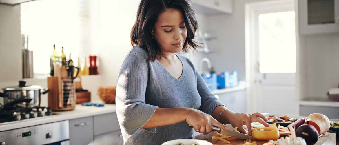 a woman cutting vegetables on a cutting board in her kitchen