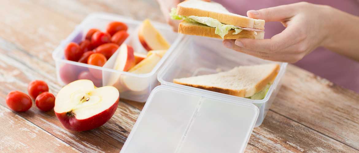 A plastic container with cut fruits and someone picking up half of a sandwich from the container