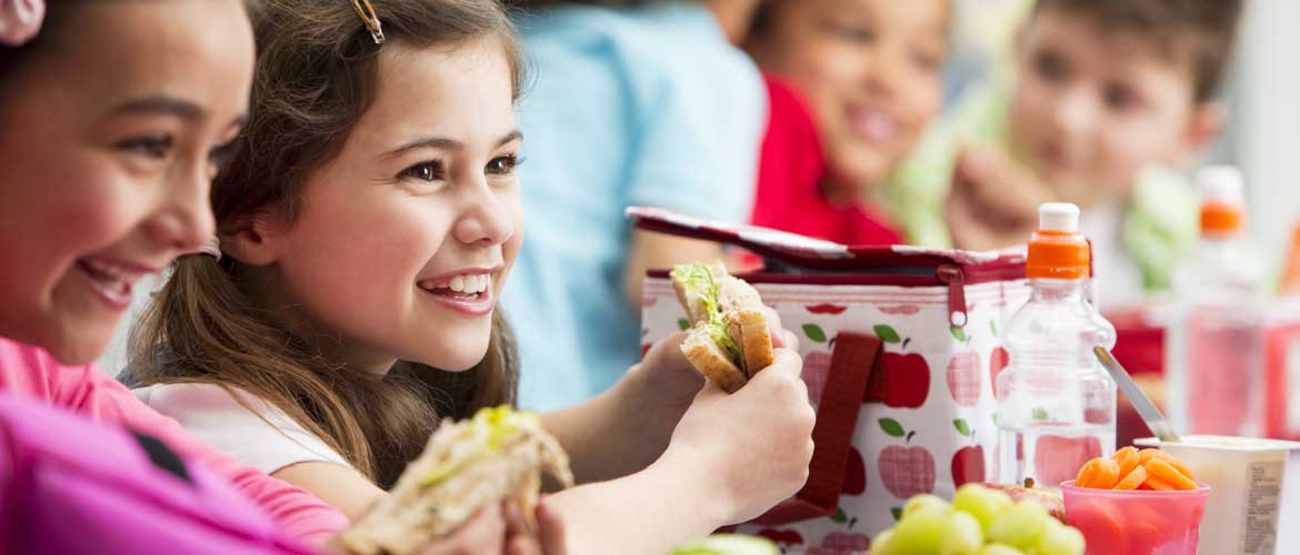 School children smiling eating their sandwiches during their school lunch break
