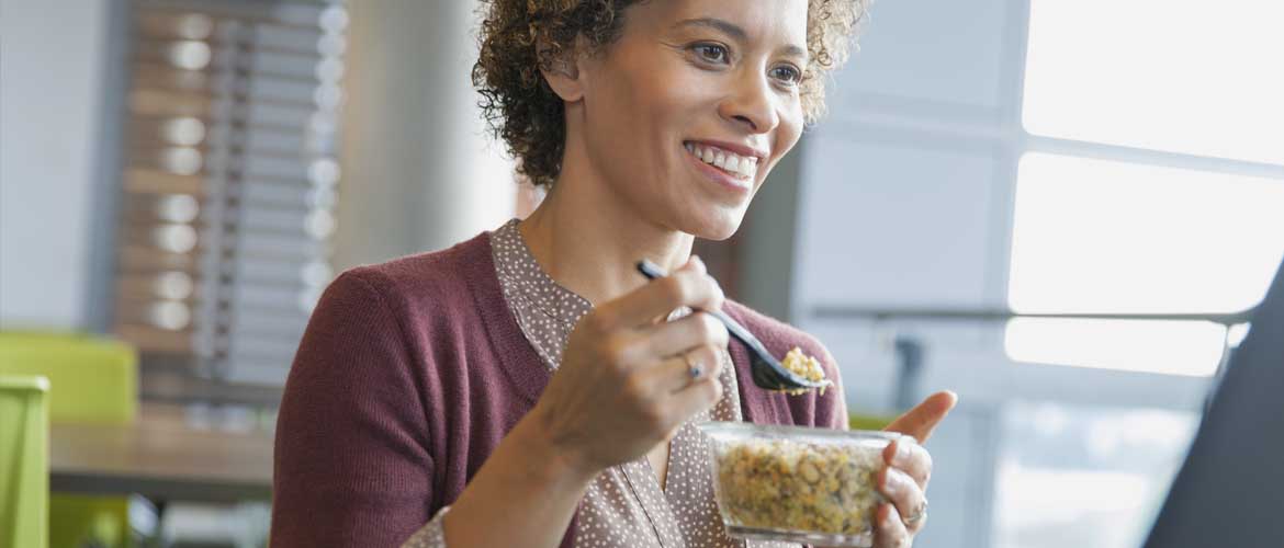 A woman at work holding a fork and eating food from a plastic container