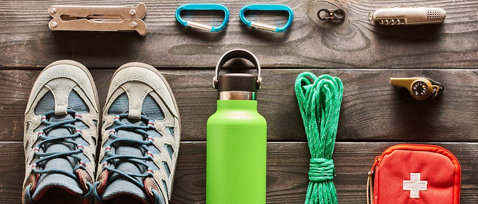 hiking gear, including a water bottle, sneaker, and first-aid kit, laid out on a wood table