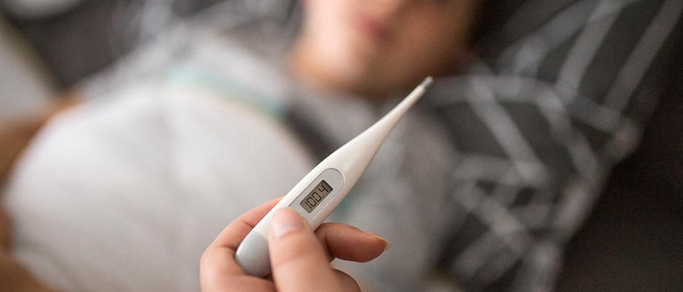 a mother holding a thermometer reading one-hundred-point-four degrees as her sick child lies in bed