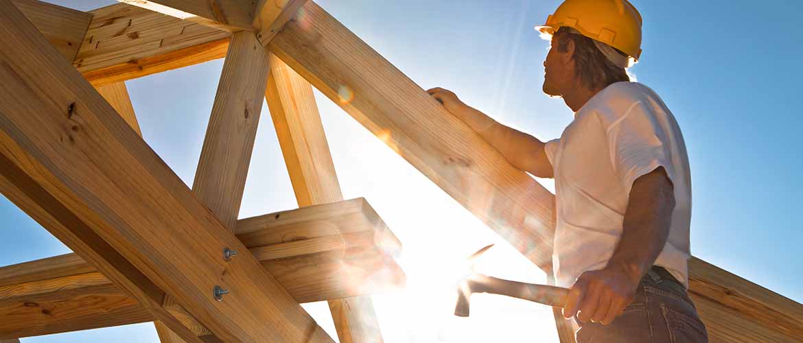 a construction worker standing outside in the frame of a house with a hammer in his hand