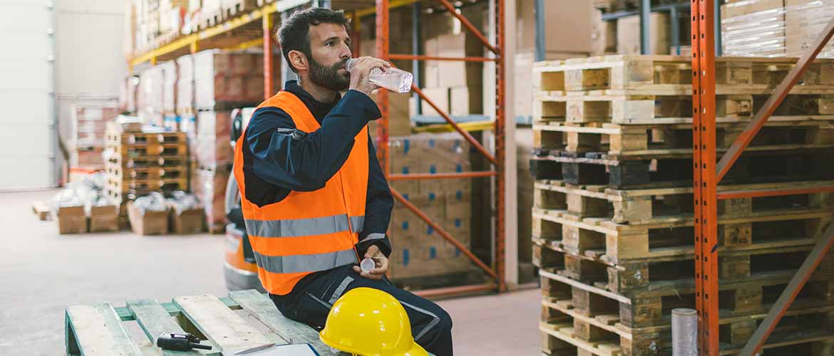 a warehouse worker sitting on a wooden crate drinking a bottle of water