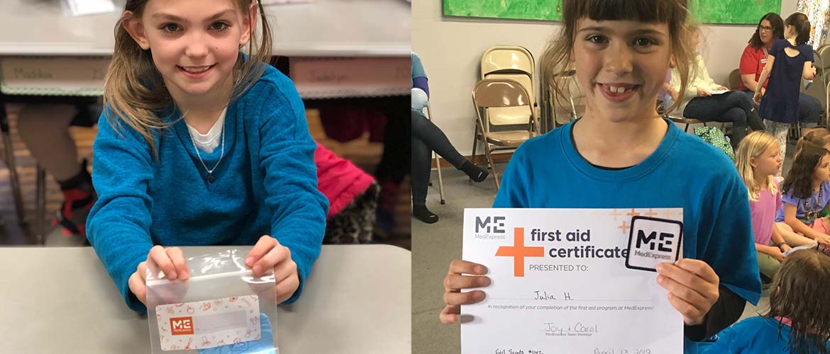 one young girl holding up a first-aid kit and another young girl holding up her first-aid kit completion certificate