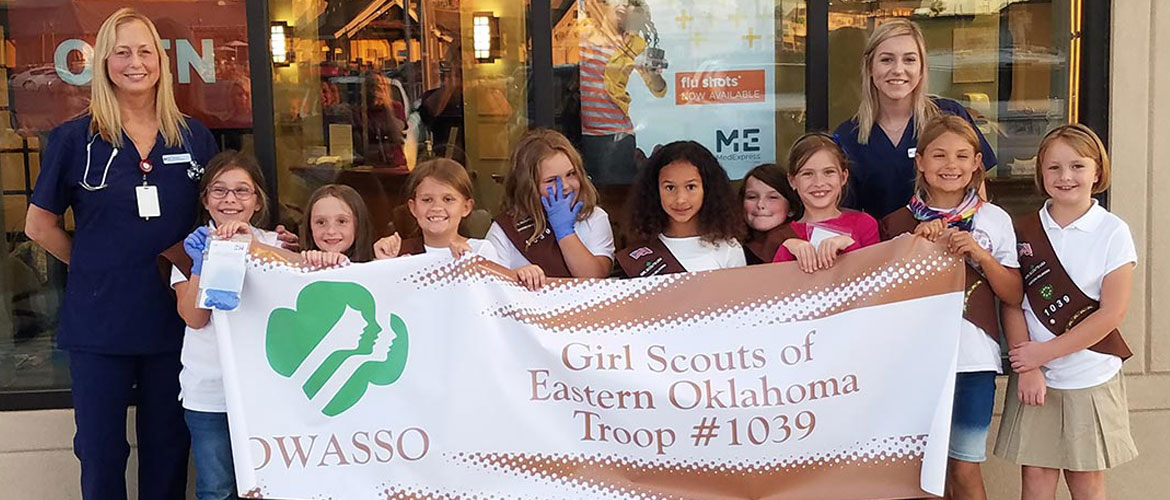 a Girl Scouts troop standing outside a MedExpress building with two MedExpress team members