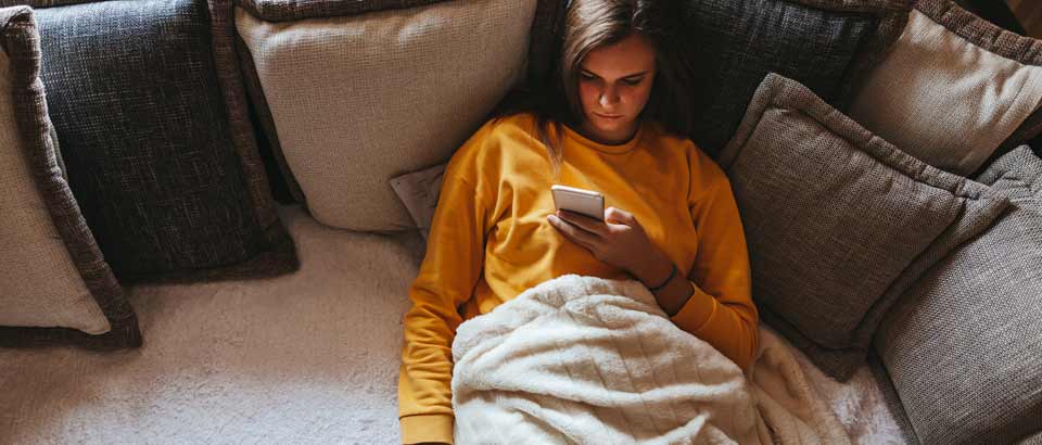 a woman sitting on her couch scrolling through her phone