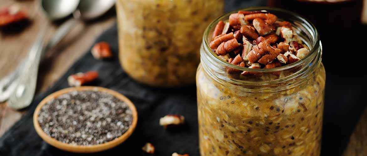 a mason jar filled with oats, chia seeds, pumpkin puree, and Greek yogurt and topped with nuts sitting on a table