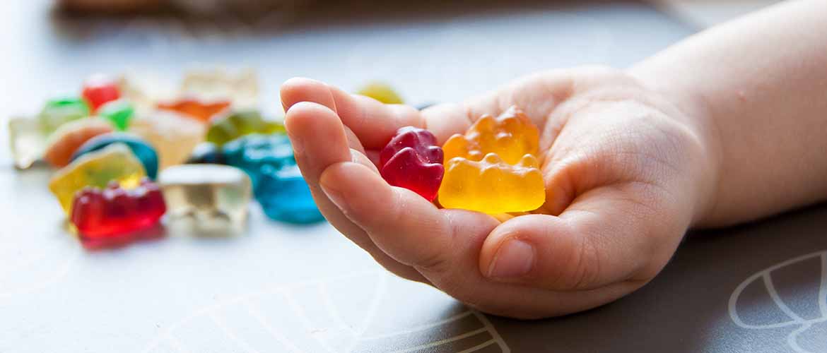 a hand holding several gummy bears with more gummy bears nearby
