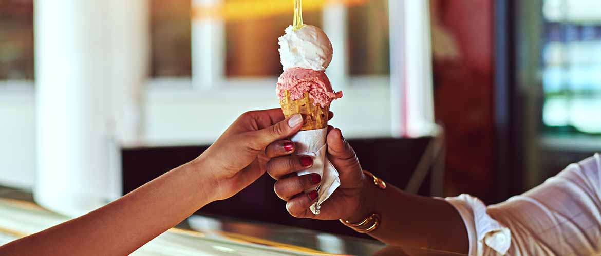 an ice cream shop employee handing an ice cream cone to a customer