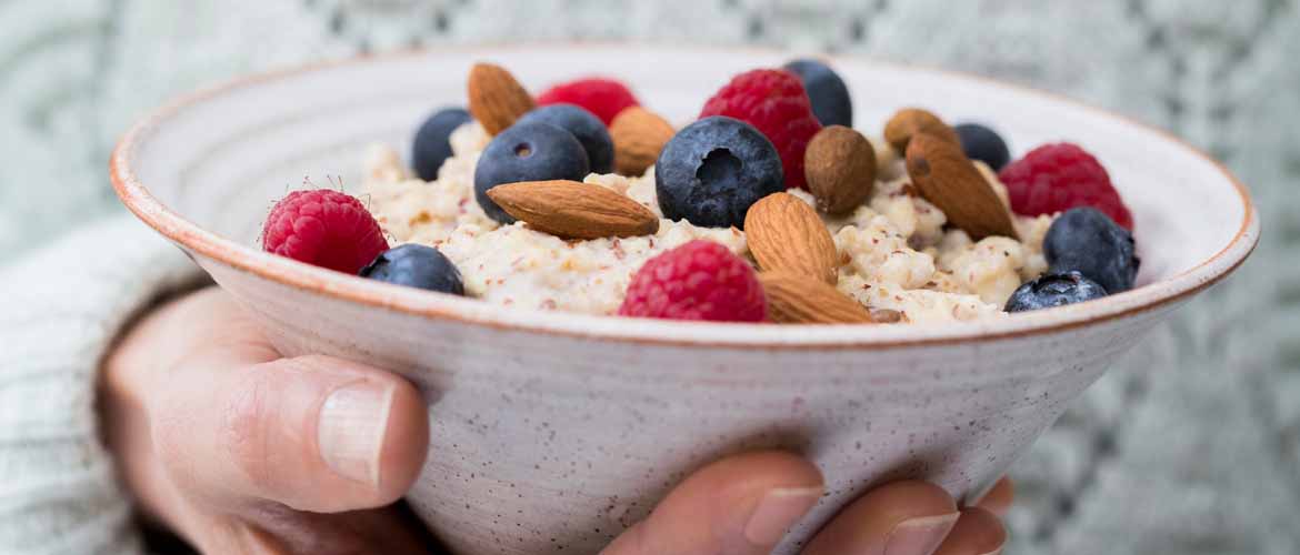 a person holding a bowl of oatmeal with berries and nuts on top