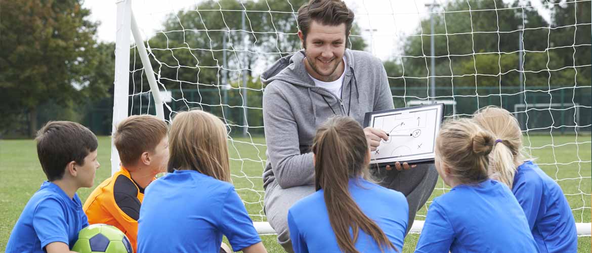 young soccer players sitting before their coach as he explains a play drawn on a whiteboard