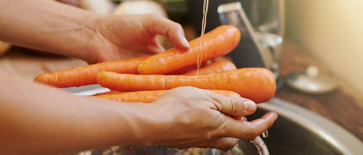 a person washing carrots over a sink