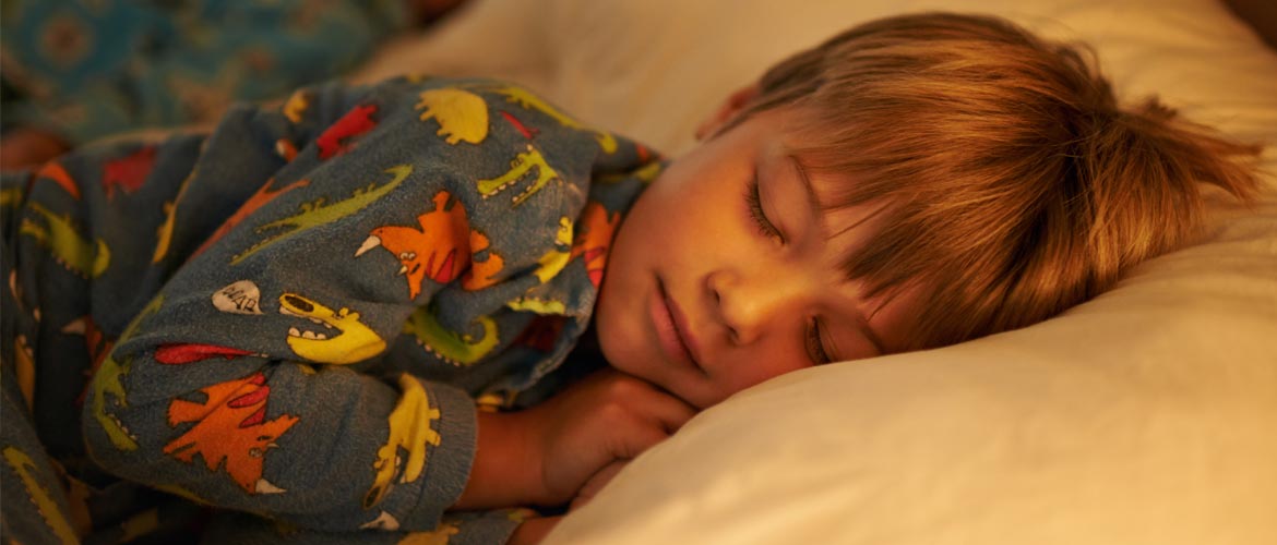 A young boy in his pajamas lying down on his belly with his eyes closed and faced snuggled against his pillow