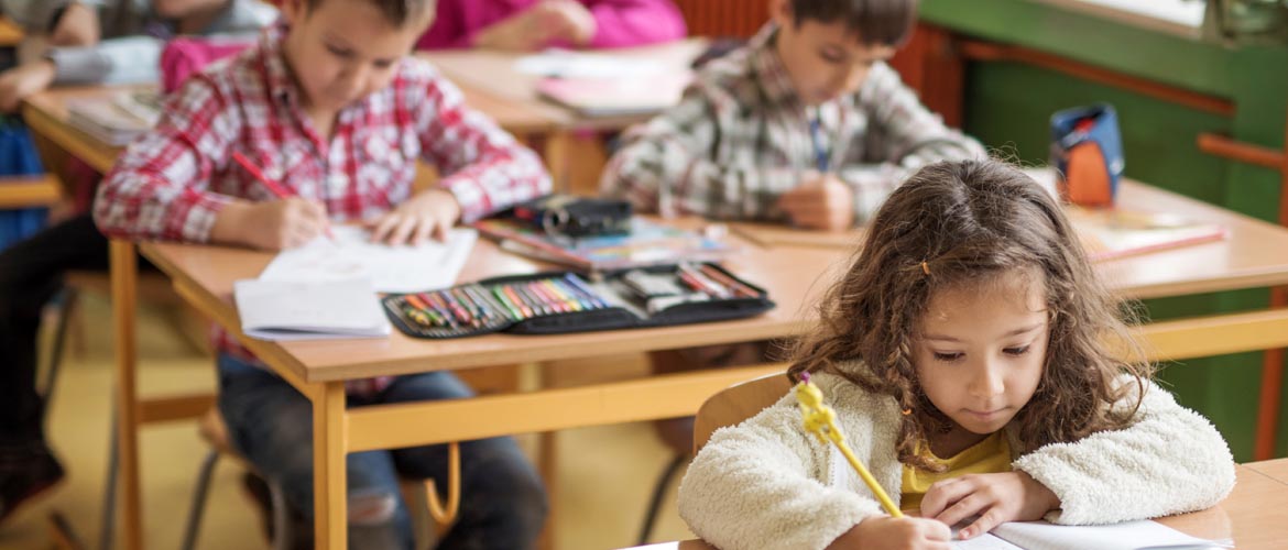 School kids at their desks working on schoolwork with pencils and crayons