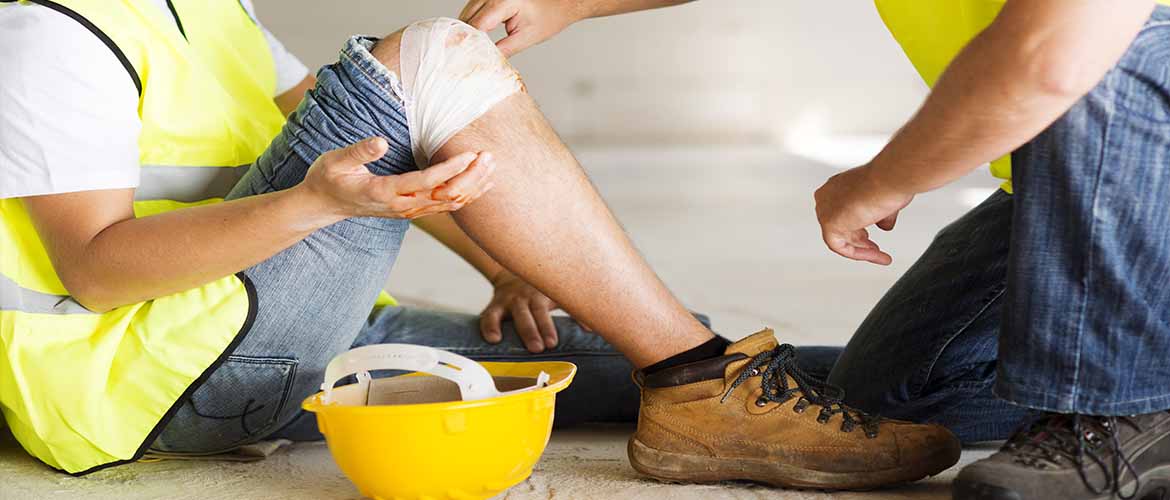 a coworker tends to a construction worker who has an injured knee