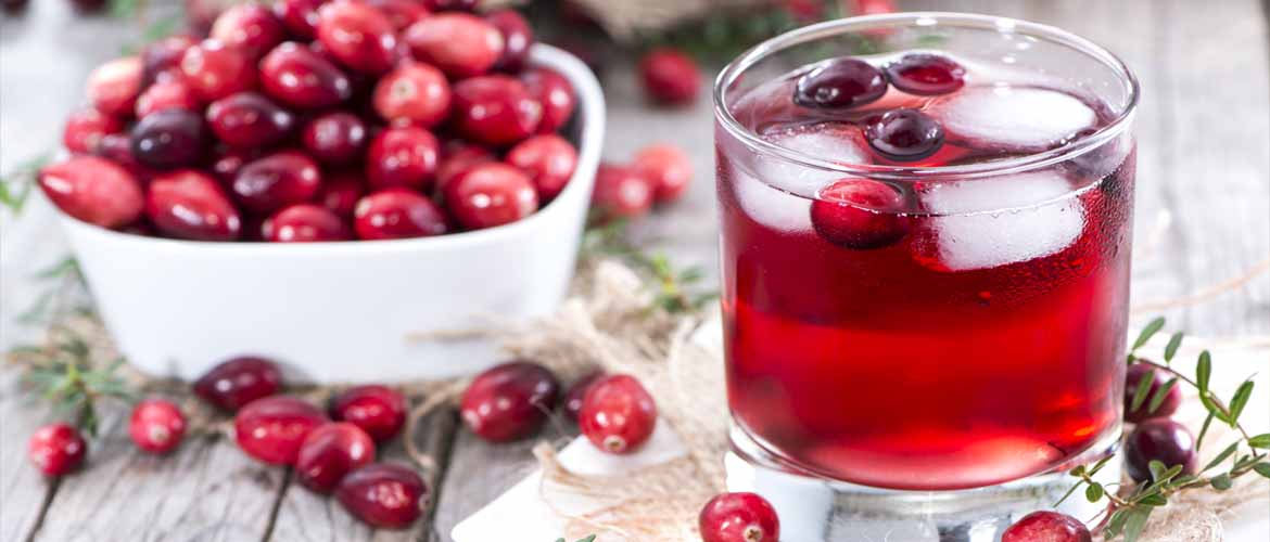 a bowl of cranberries sitting next to a glass of cranberry juice