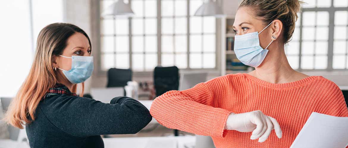 two female office employees bumping elbows while wearing face masks and gloves