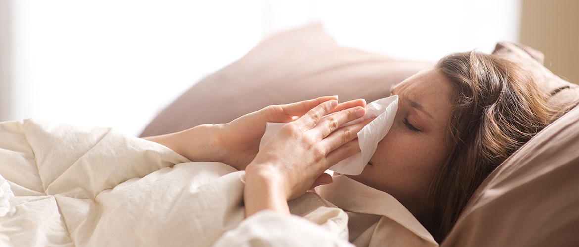 a woman laying in bed blowing her nose into a tissue